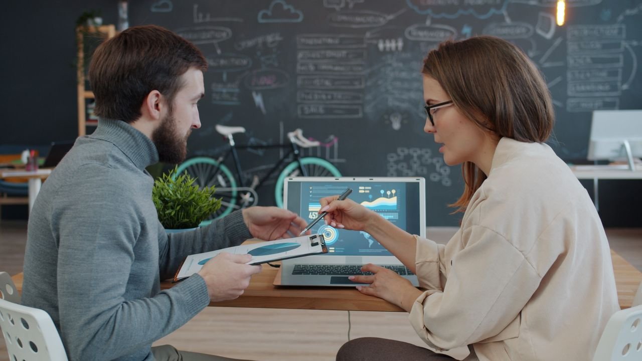 Two professionals discussing data analytics on laptop in creative office.